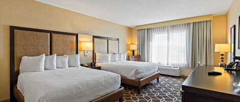 A hotel room with two beds, a desk, and a large window with curtains.