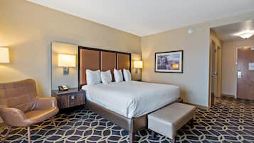 A hotel room with a large bed, a chair, a desk with a phone, and a picture on the wall.
