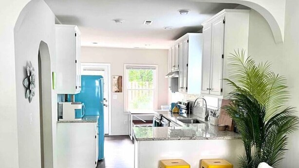Una cocina moderna con armarios blancos, una encimera azul y una isla central con taburetes.