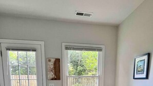 Una habitación pequeña y luminosa con una puerta blanca, una ventana que da a una valla de madera y una mesa blanca con un banco.