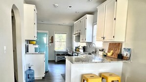 Una cocina moderna con armarios blancos, encimera de granito y dos taburetes amarillos.