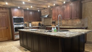A kitchen with dark wooden cabinets, a granite countertop, stainless steel appliances, and a large island with a sink. - RAIN VALLEY RETREAT on 6 STUNNING acres! GAMES/GRILL/AC! (Flagstaff)