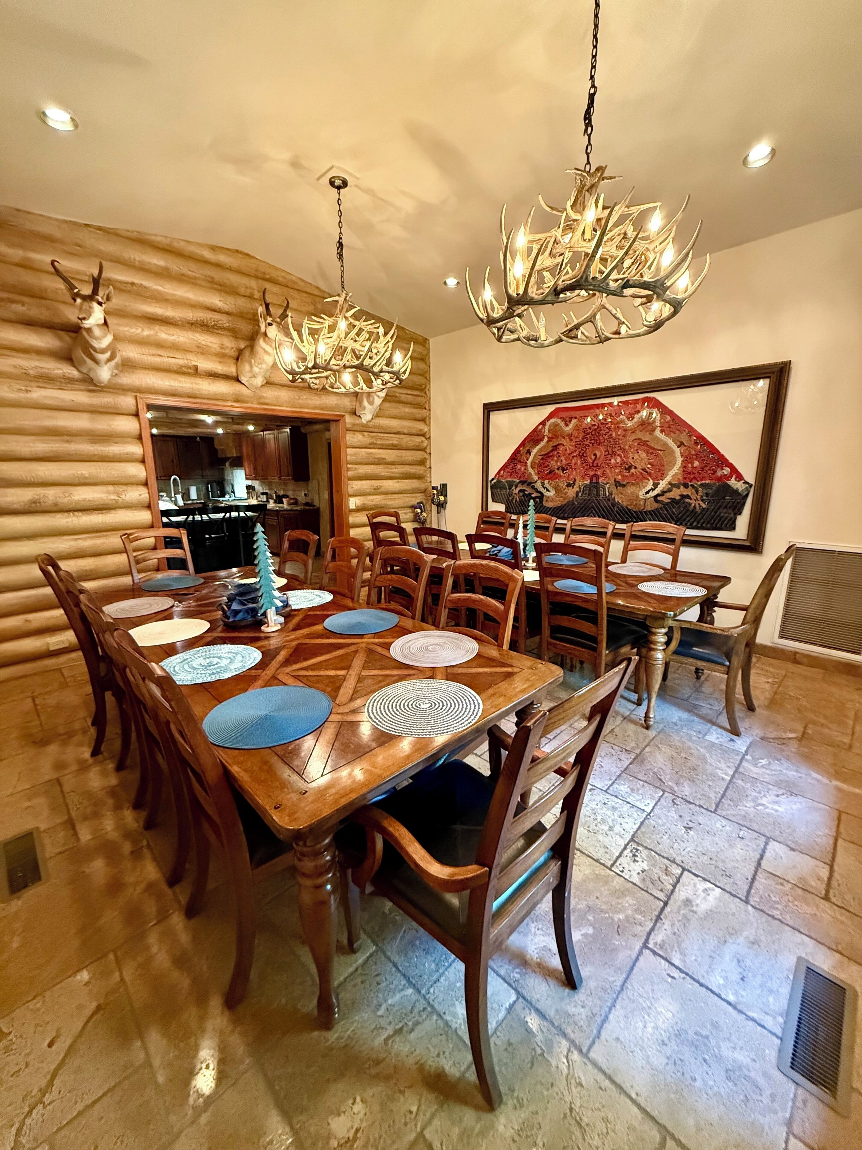 A dining area with a wooden table set for six, surrounded by chairs, and two chandeliers.