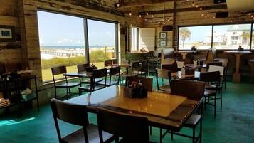 A restaurant with a rustic interior, large windows offering a view of the beach, and multiple seating areas.