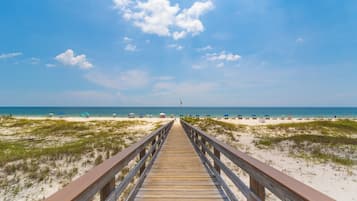 A wooden boardwalk leading to a beach with umbrellas and people.