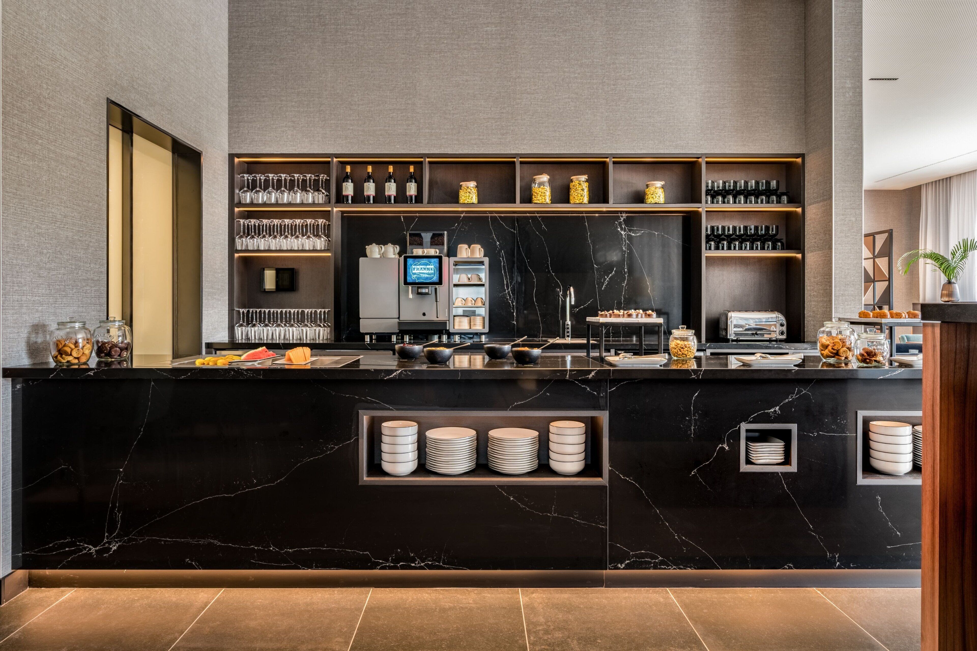 A modern bar area with a marble countertop, shelves with glassware, and a television.