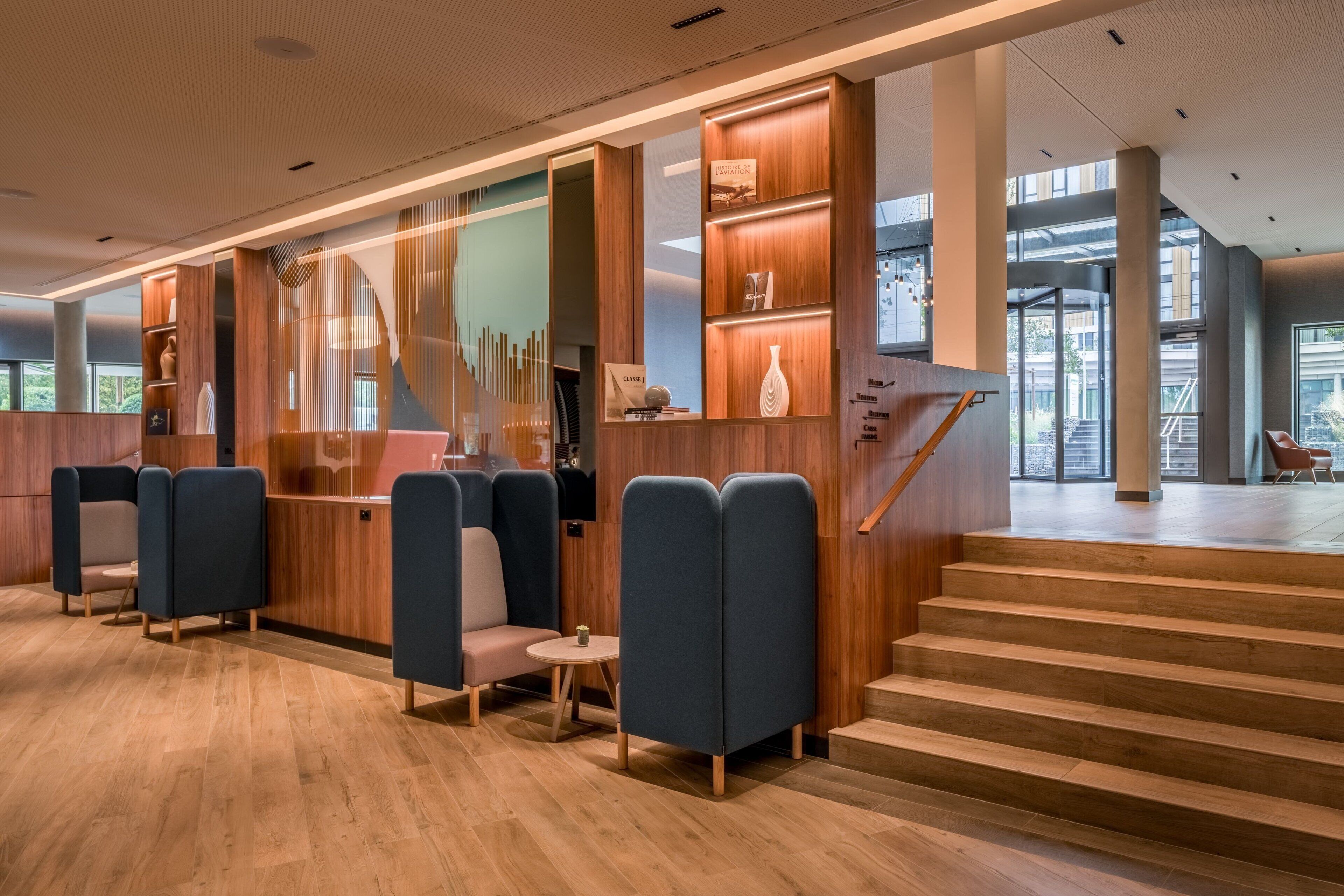 Un lobby moderno con paneles de madera, zonas de estar y una escalera que conduce a un nivel superior.