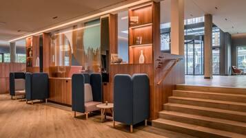 Un lobby moderno con paneles de madera, zonas de estar y una escalera que conduce a un nivel superior.