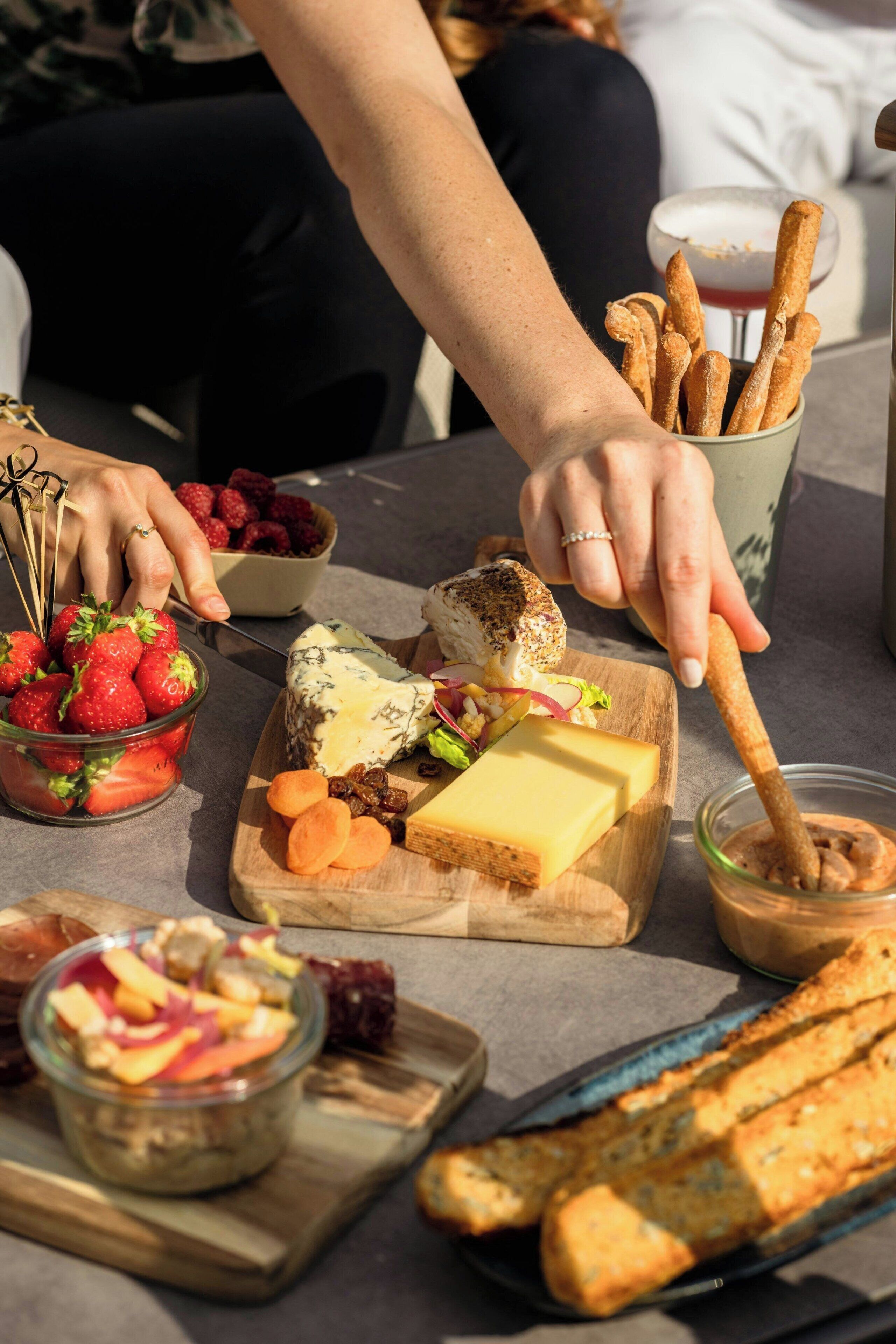 Una mesa con diversos alimentos, como fresas, queso y palitos de pan.