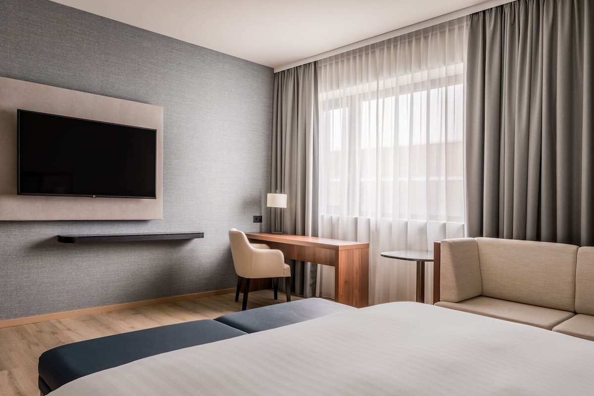 Une chambre d’hôtel moderne avec un grand lit, un bureau avec une chaise, un téléviseur fixé au mur et une fenêtre avec des rideaux.