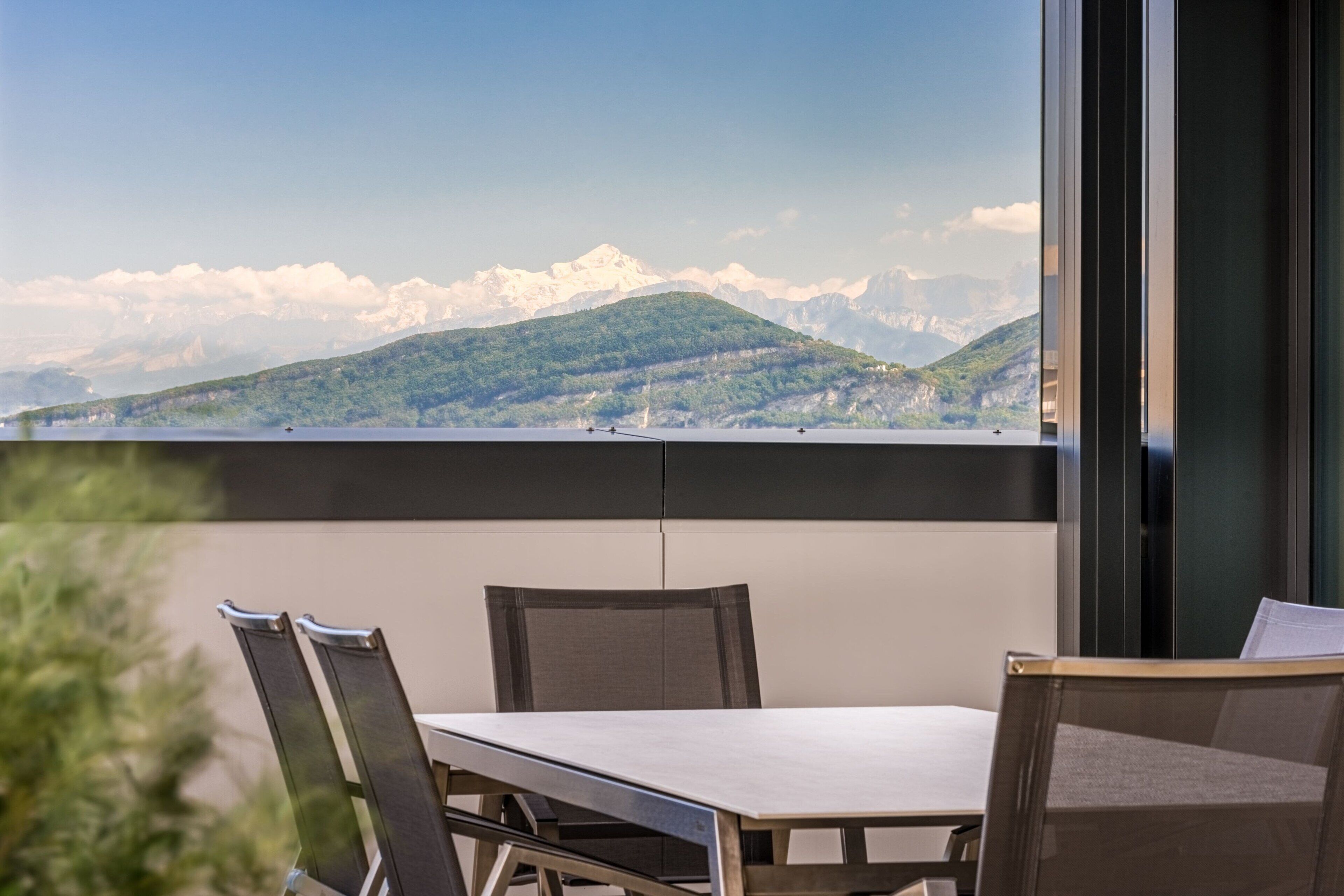 A balcony with a table and chairs, overlooking a mountainous landscape.