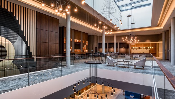 Un interior moderno con un espacio central abierto, zonas de estar y una barandilla de cristal con vistas a un nivel inferior.
