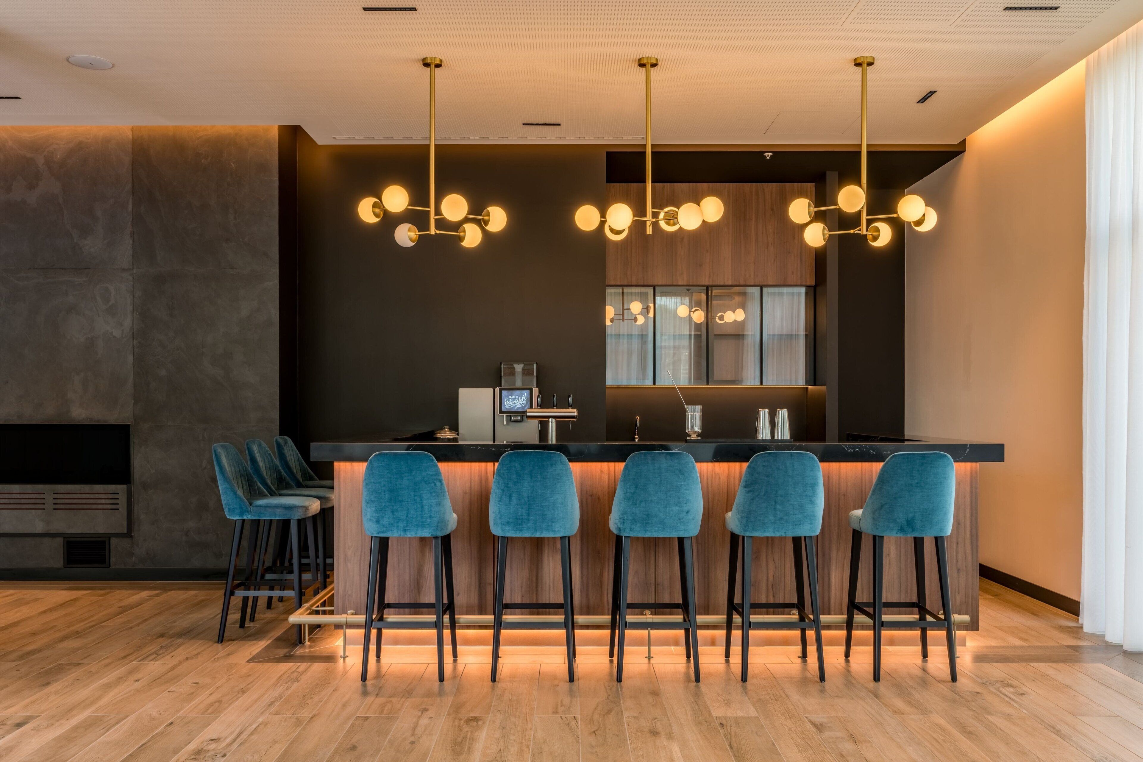 Un espace bar moderne doté d’un long comptoir, de plusieurs tabourets de bar bleus et d’un éclairage suspendu.