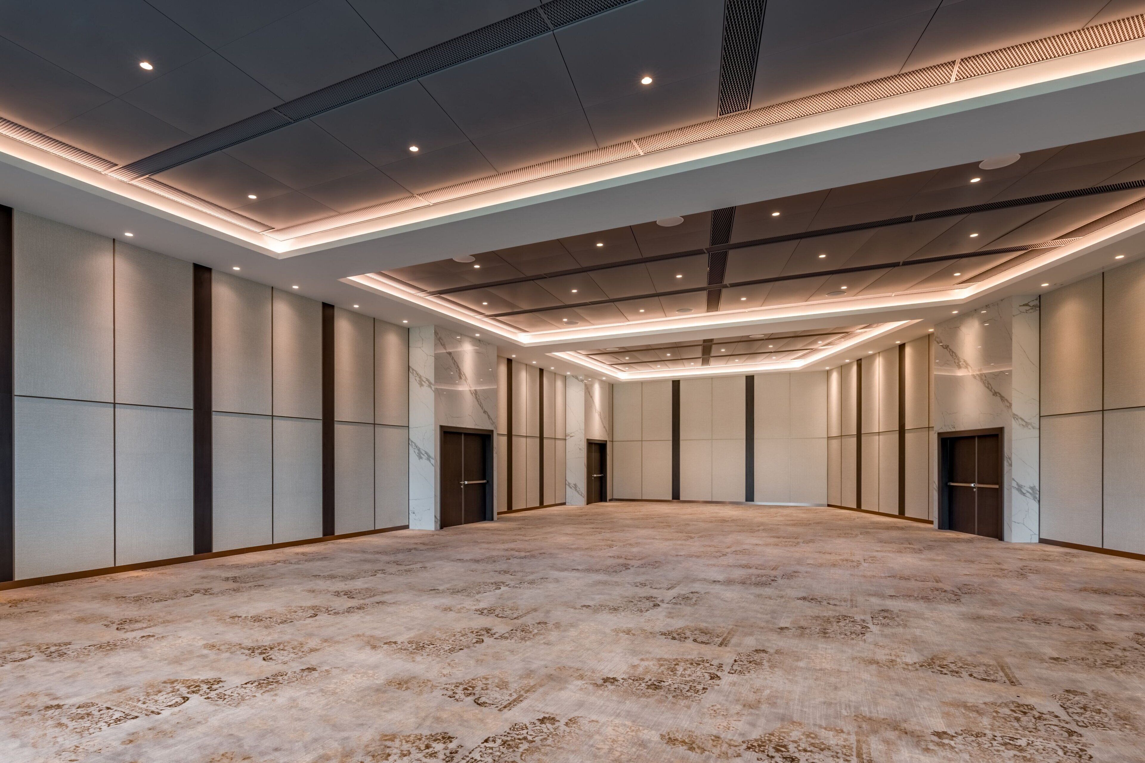 A spacious, modern hotel room with a large, carpeted floor, recessed lighting, and a minimalist design.