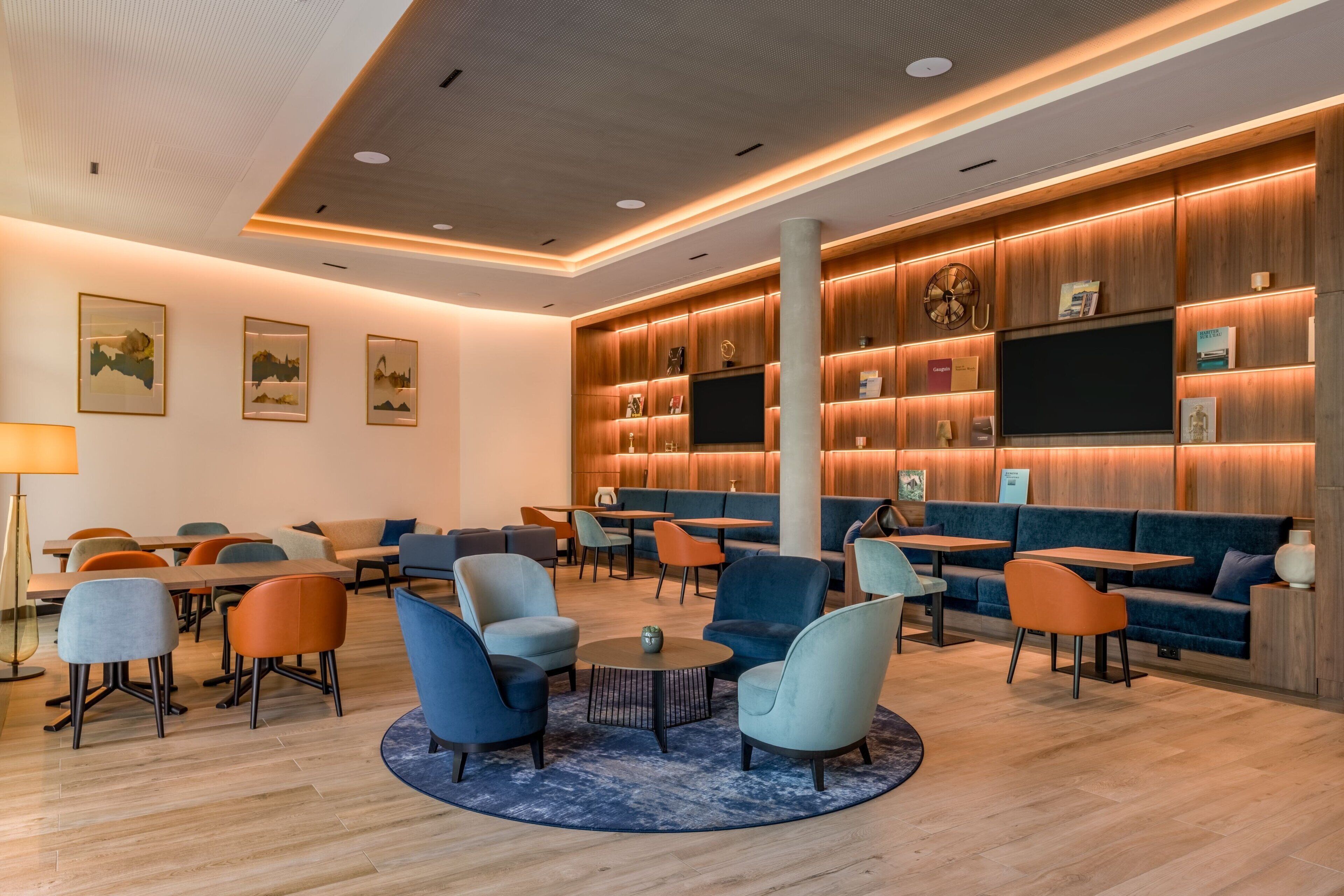A modern lounge area with seating arrangements, a central coffee table, and a wooden wall with shelves and a television.