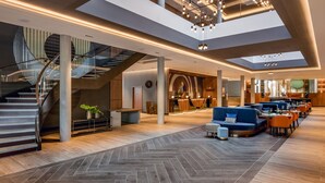 Un vestíbulo amplio con una escalera central, zonas de estar y una lámpara moderna.