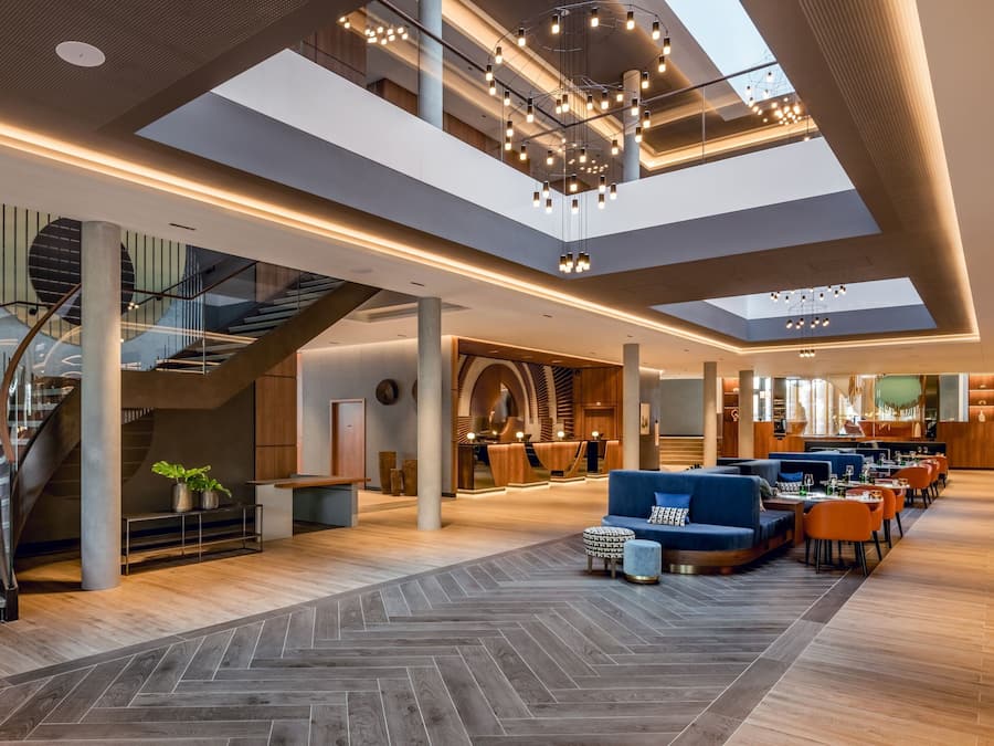 Eine großzügige Lobby mit einer zentralen Treppe, Sitzbereichen und einem modernen Kronleuchter.