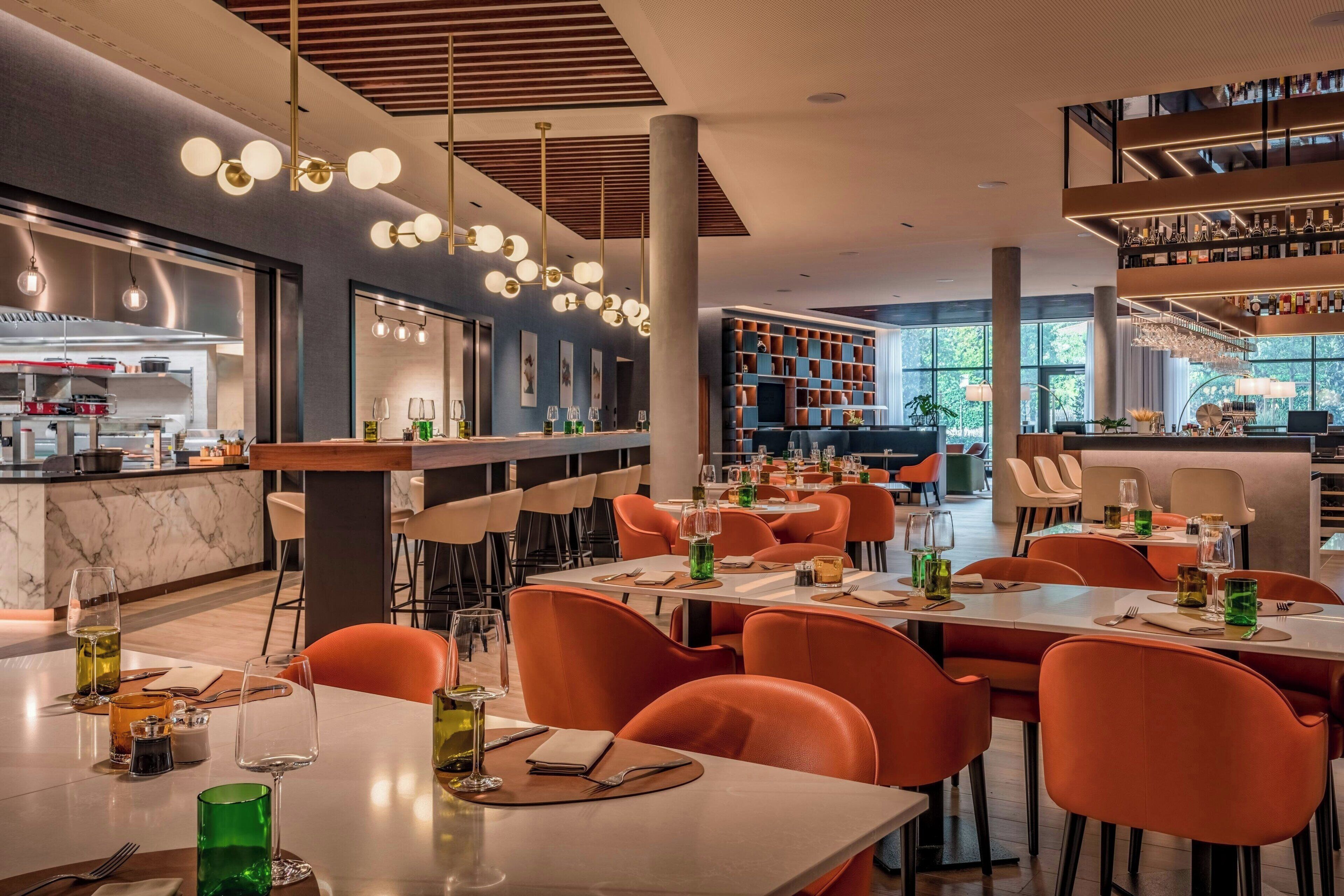 Un restaurante moderno con sillas anaranjadas, una zona de bar y una cocina visible al fondo.