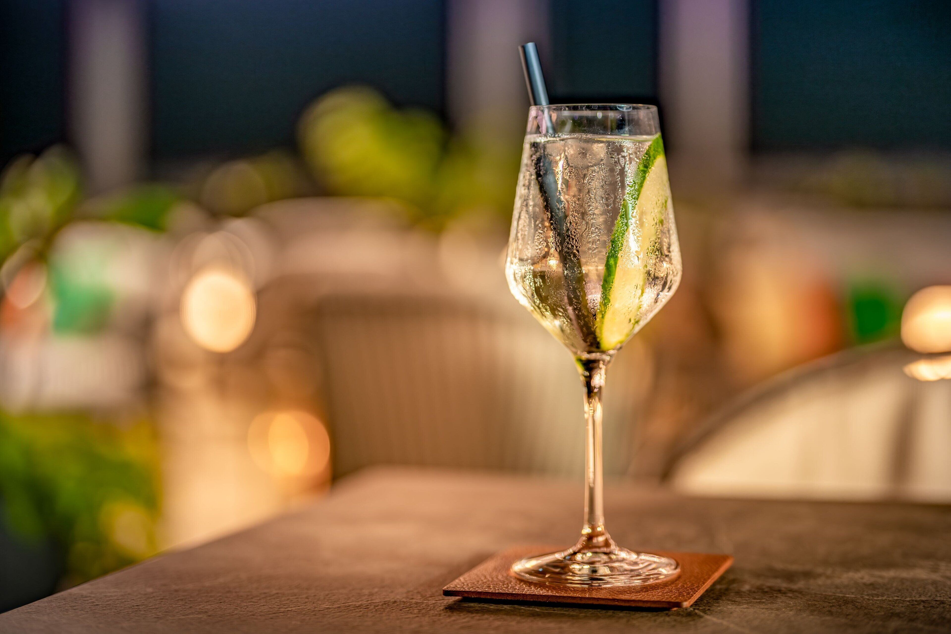 A glass of cocktail with a straw on a coaster, placed on a table.