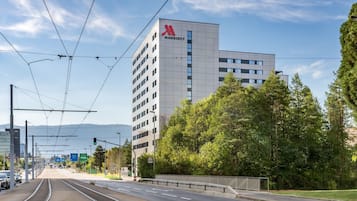A modern building with a prominent logo, likely a hotel, adjacent to a tram line and a road with traffic lights.