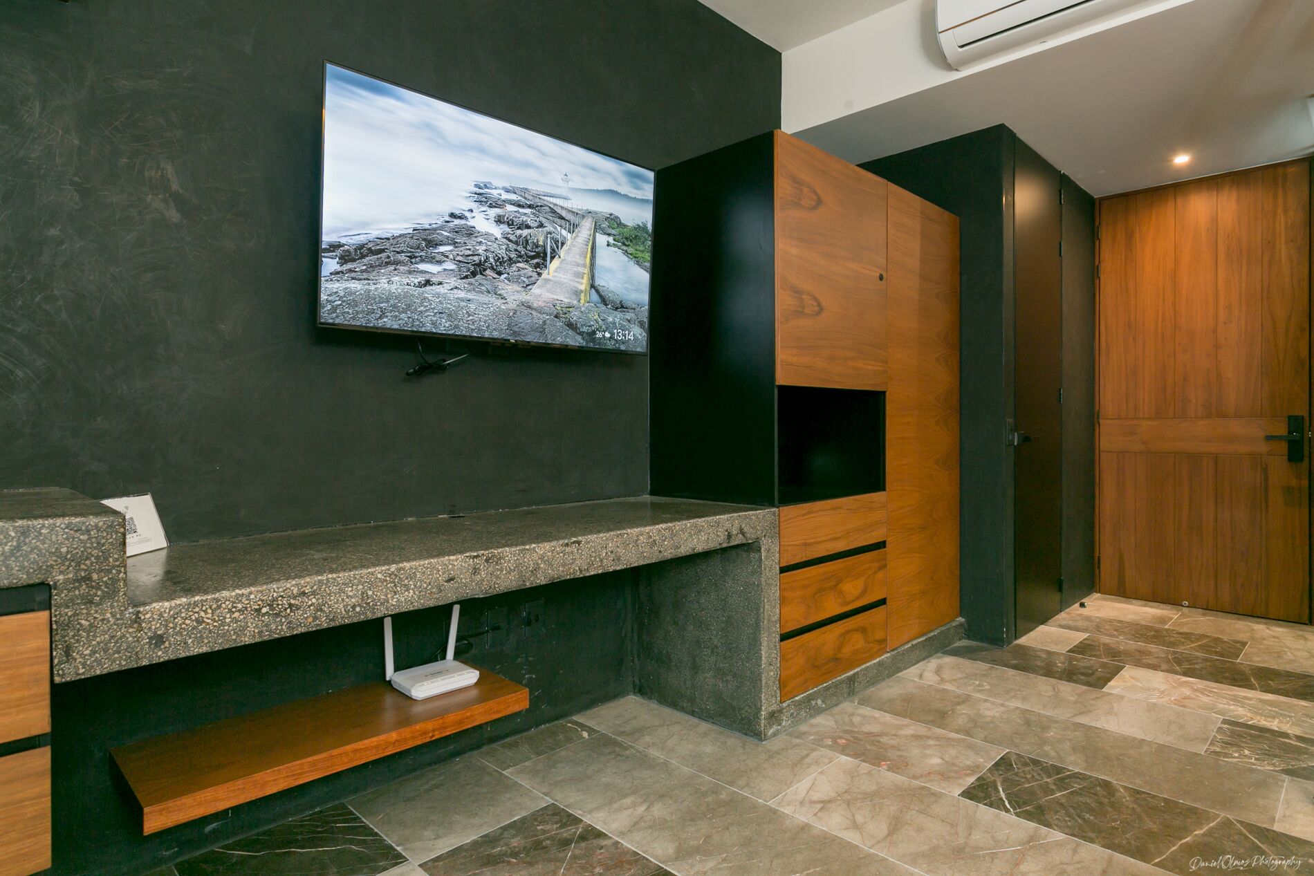 A modern bathroom with a granite countertop, a mounted TV, and wooden cabinetry.
