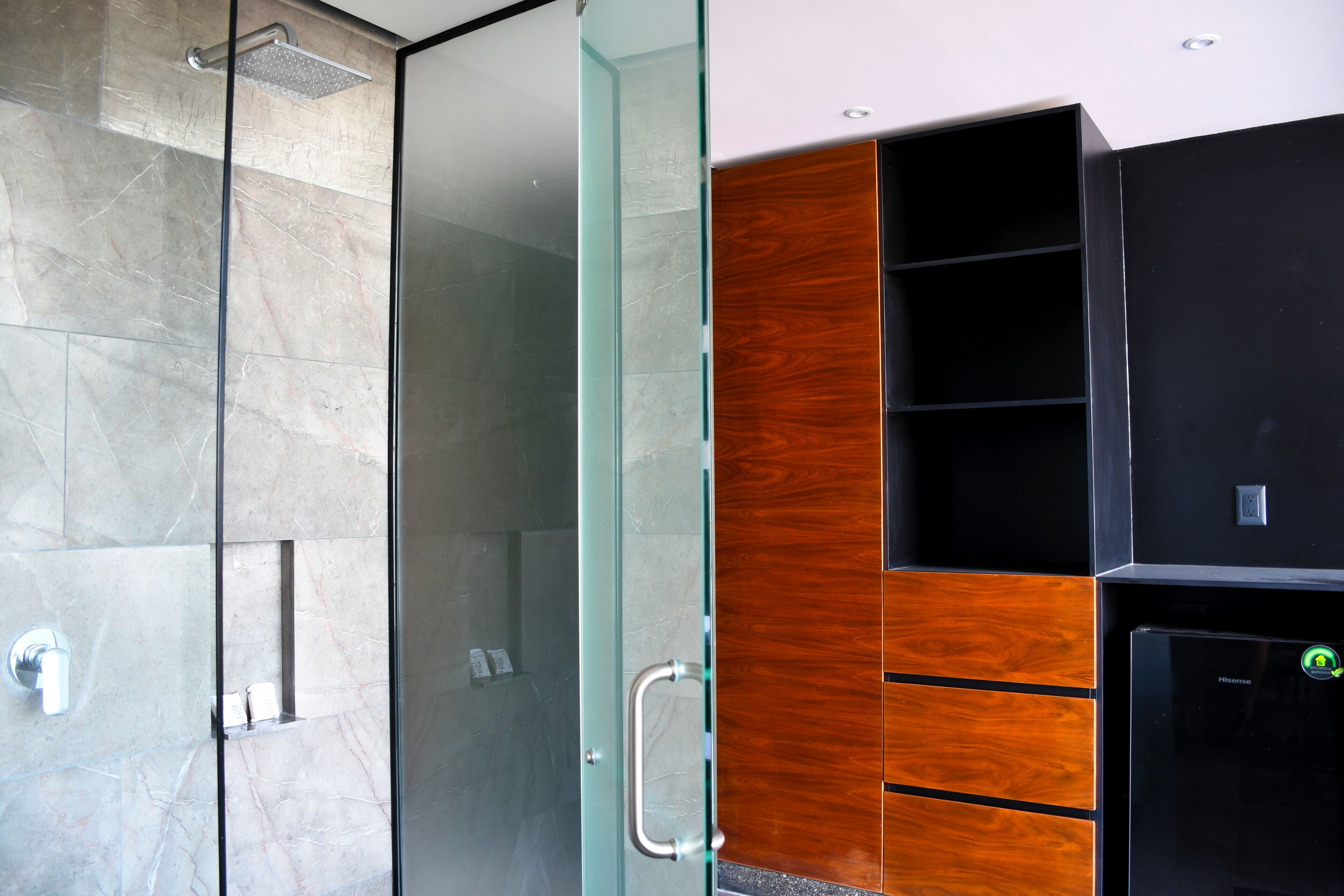 A modern bathroom with a glass shower enclosure, a wooden vanity, and a black refrigerator.