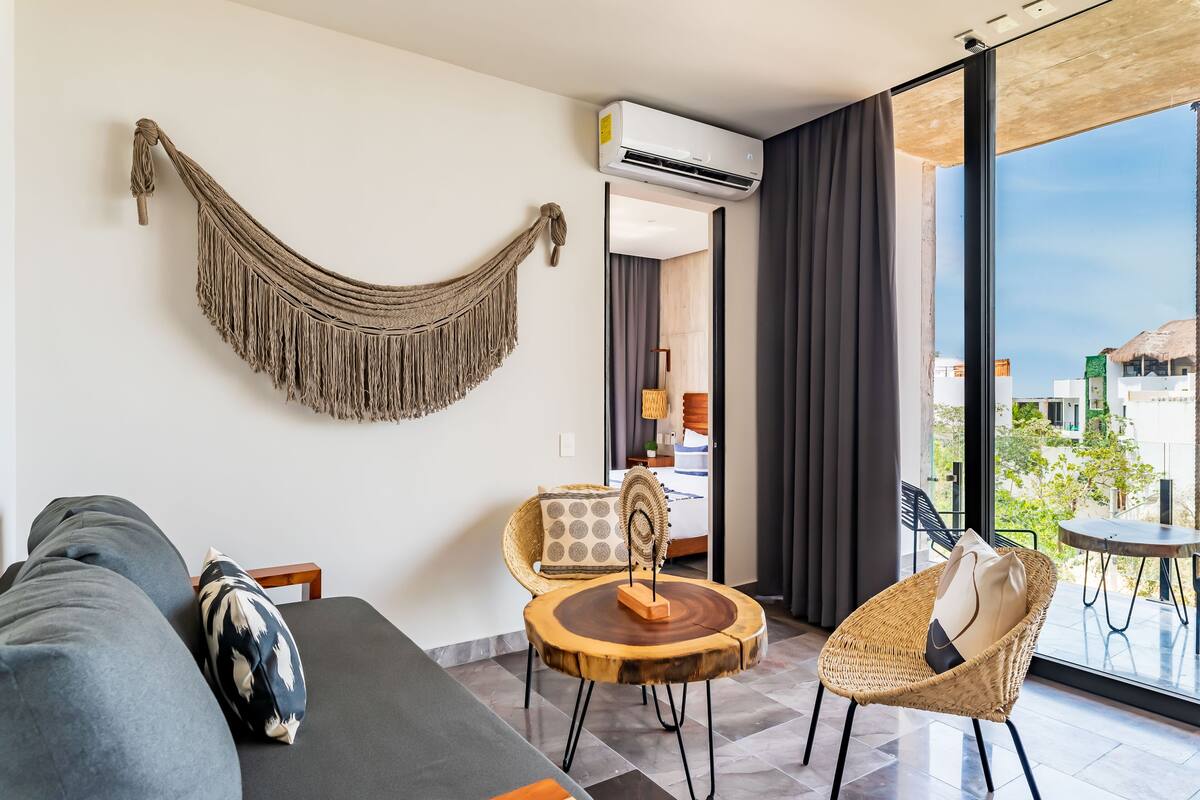 A modern living room with a hammock, a sofa, a round wooden table, and a wicker chair.