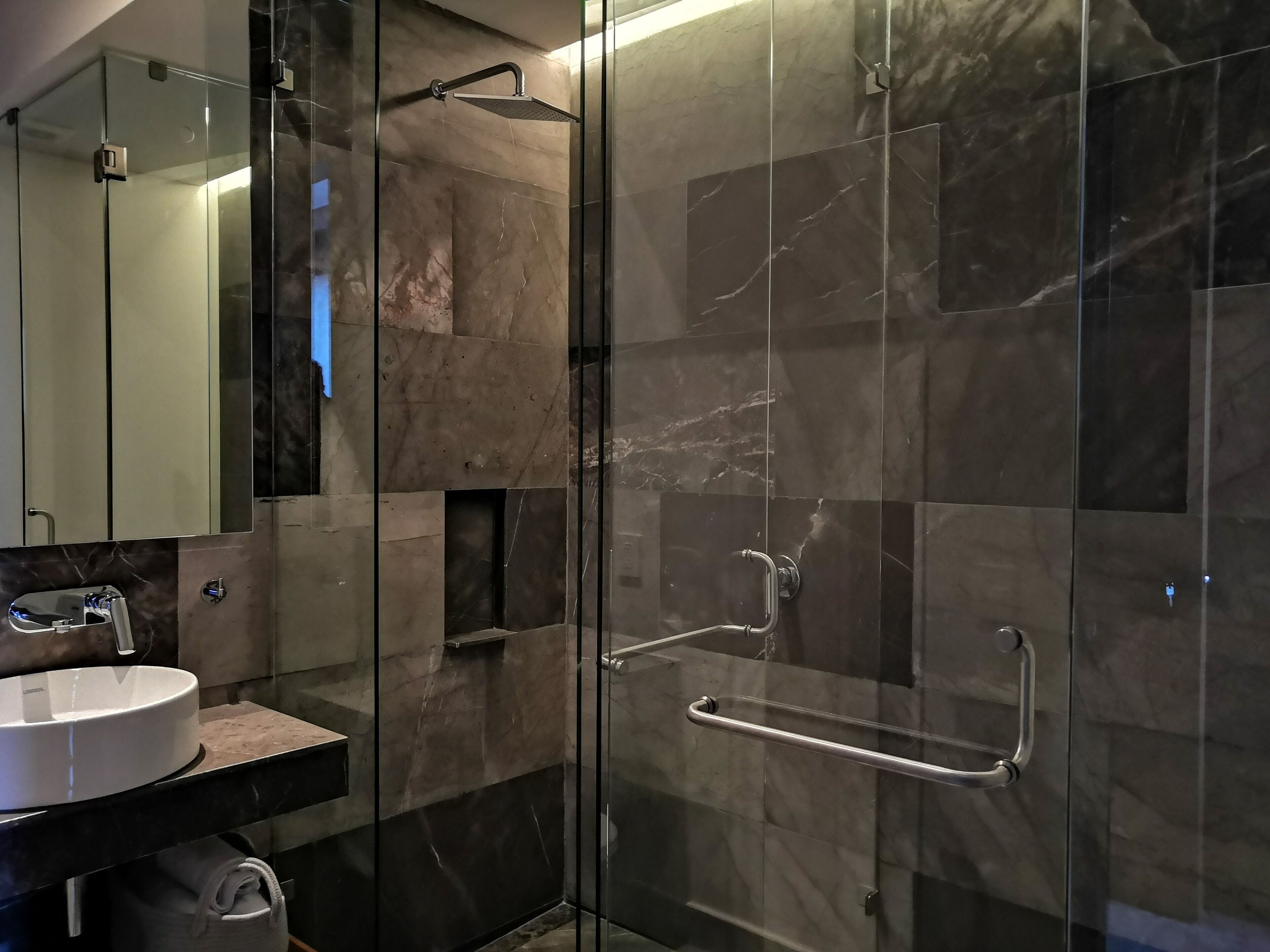 Un baño moderno con ducha de vidrio, lavamanos blanco y pared con azulejos de mármol.