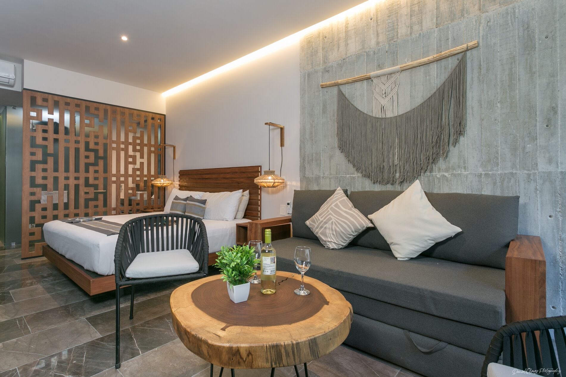 Et moderne hotelværelse med en seng, en sofa, et rundt træbord med en plante og en dekorativ vægophæng.