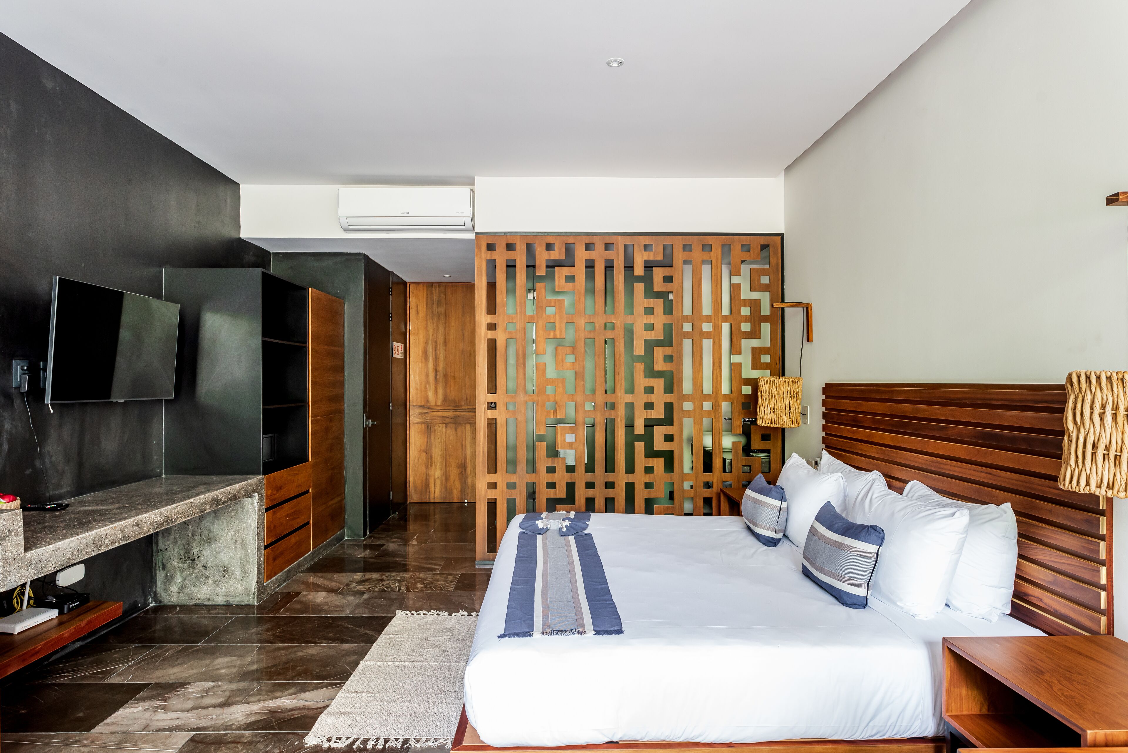A modern hotel room with a large bed, a flat-screen TV, a wooden partition, and a small desk area.
