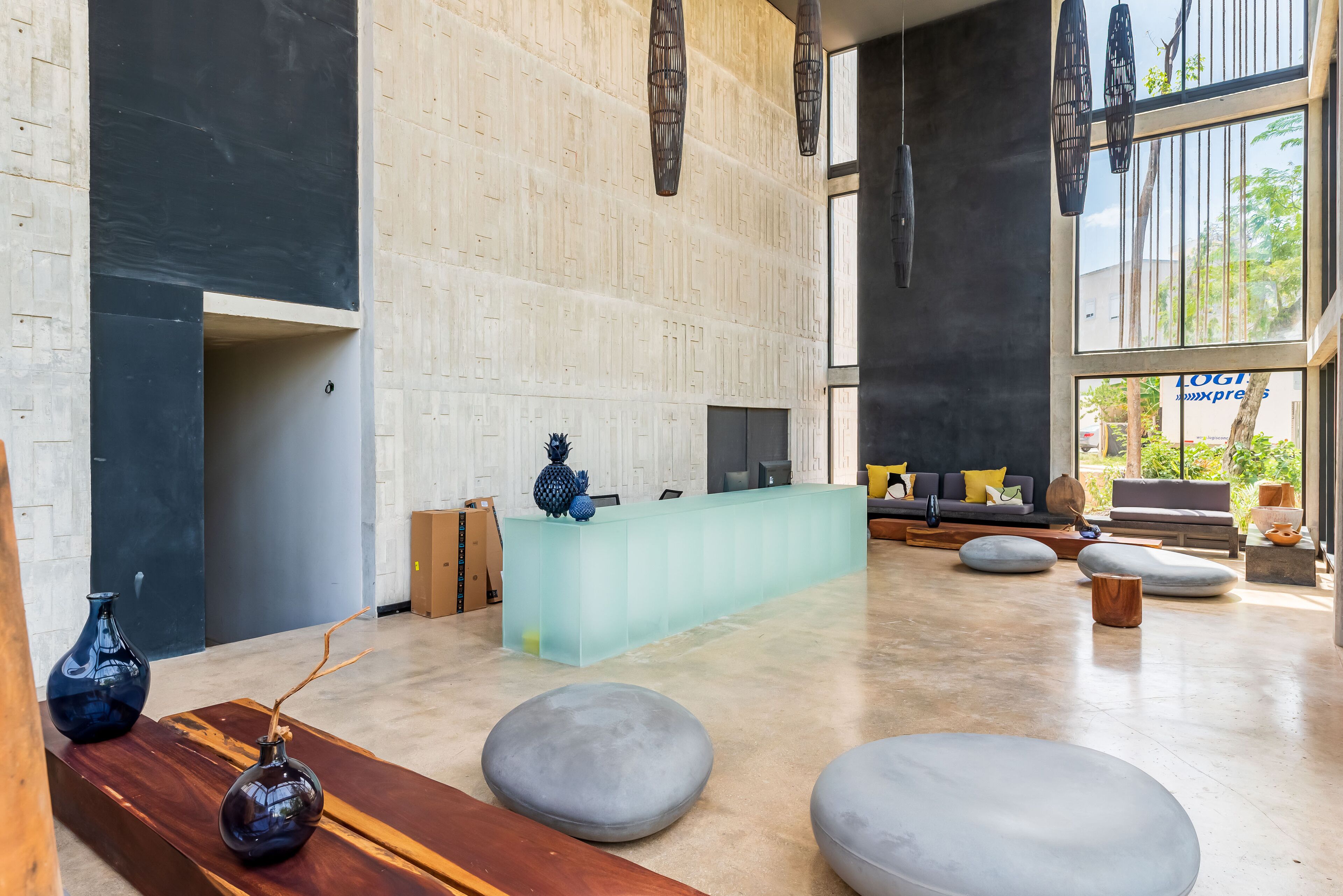 A modern reception area with a light-colored reception desk, grey seating, and a large window offering a view of greenery outside.