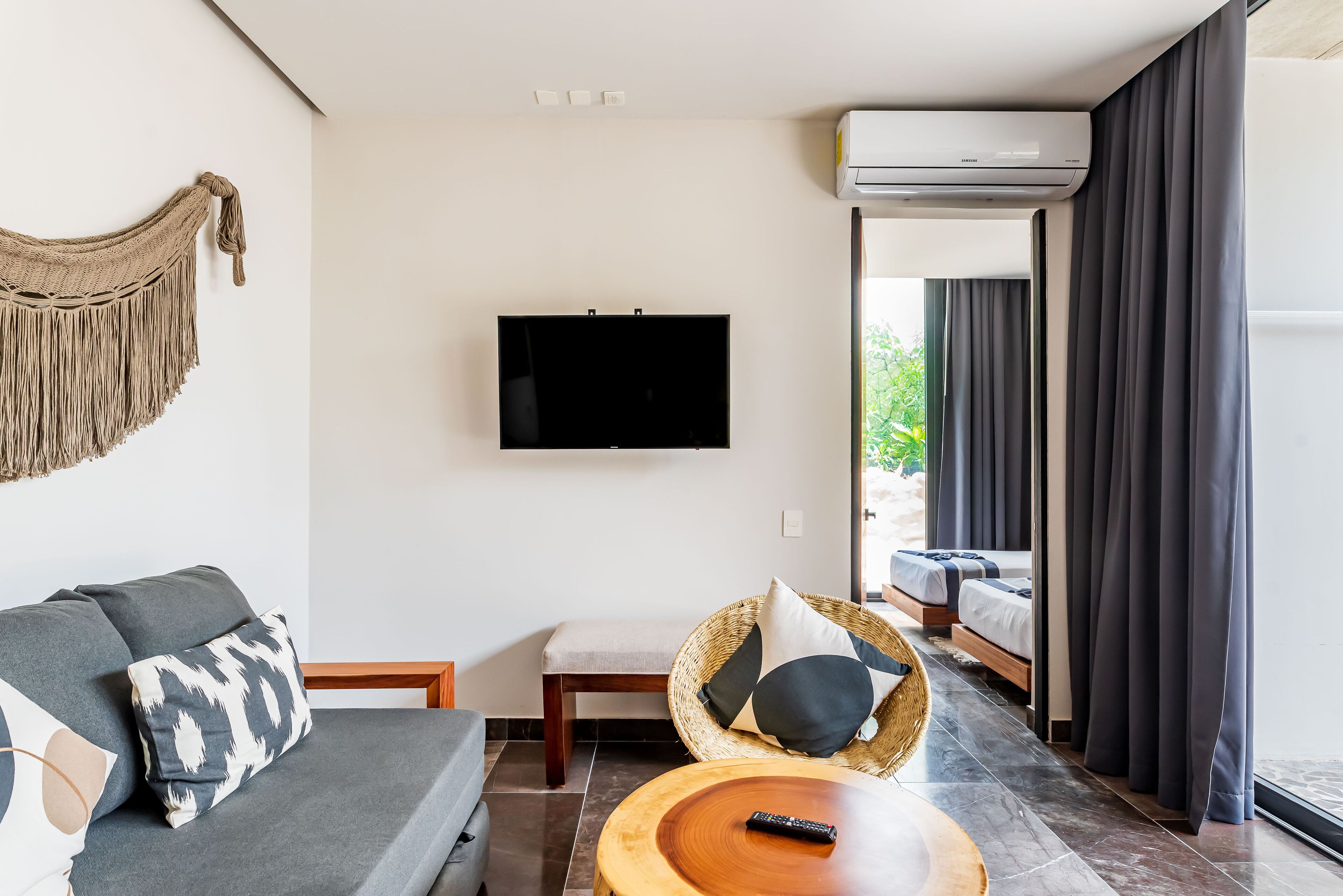 A modern living room with a flat-screen TV, a sofa, a wicker chair, and a wooden coffee table.