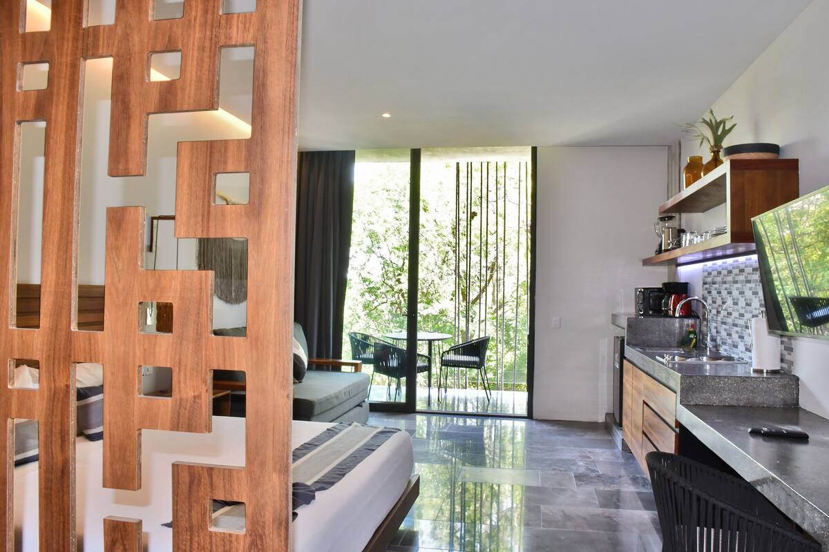 A modern kitchen with a dining area, a sofa, and a large sliding glass door leading to an outdoor space.