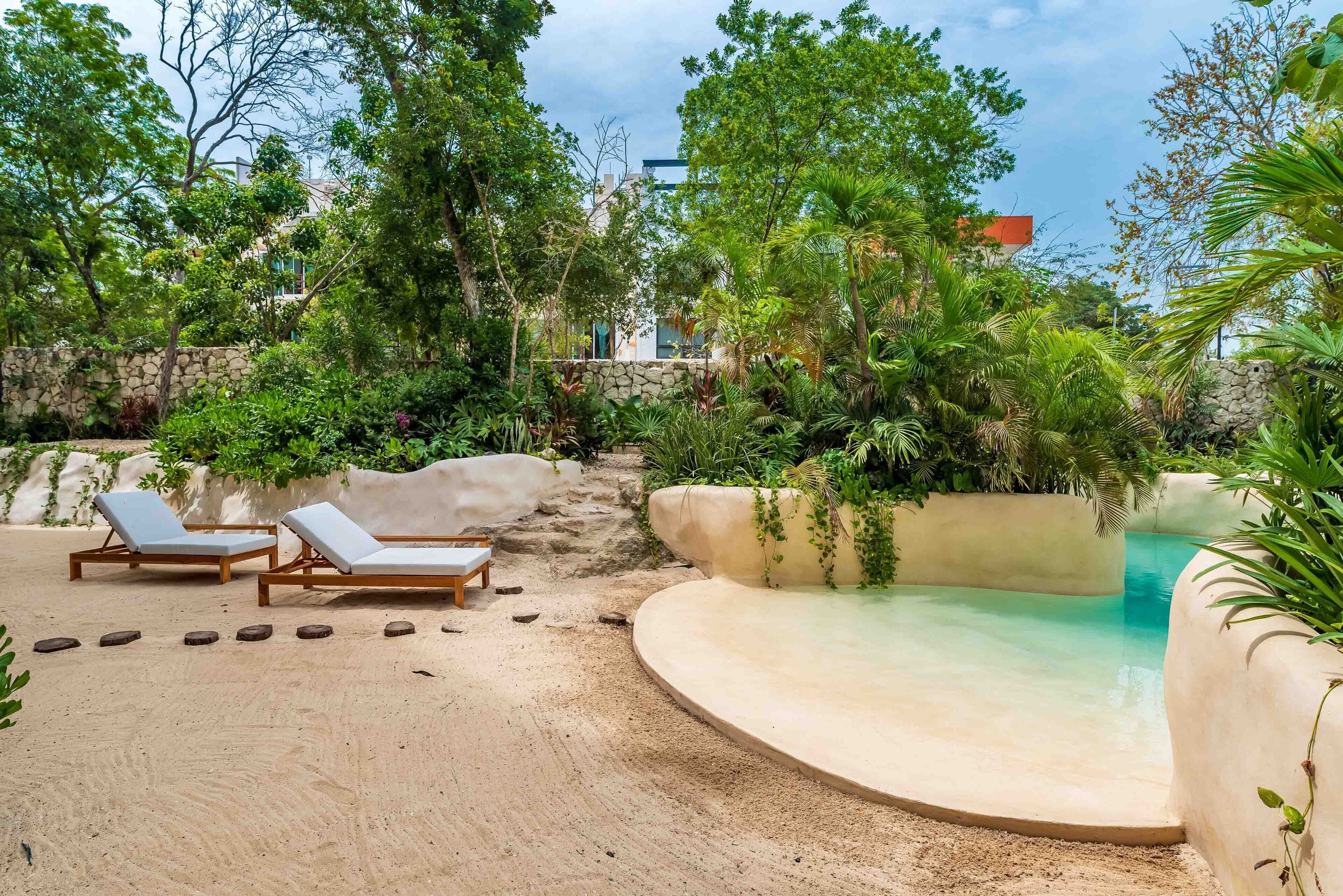 A pool area with lounge chairs, surrounded by lush greenery and a stone wall.