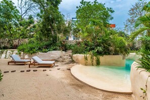 A pool area with lounge chairs, surrounded by lush greenery and a stone wall.