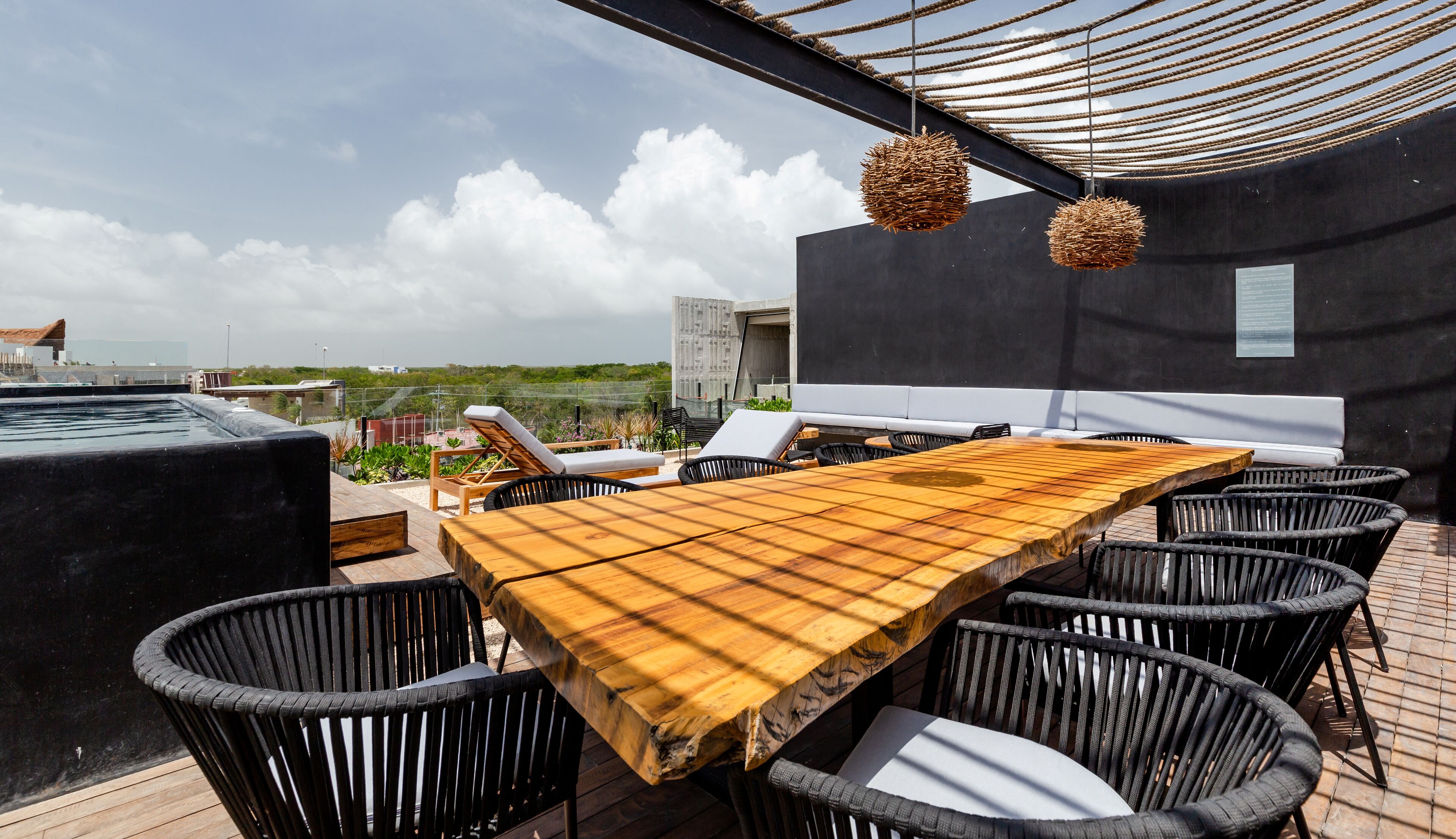 A rooftop terrace with a wooden table, black wicker chairs, and a white sofa.