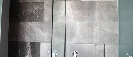 A bathroom with a tiled wall and a glass shower enclosure.