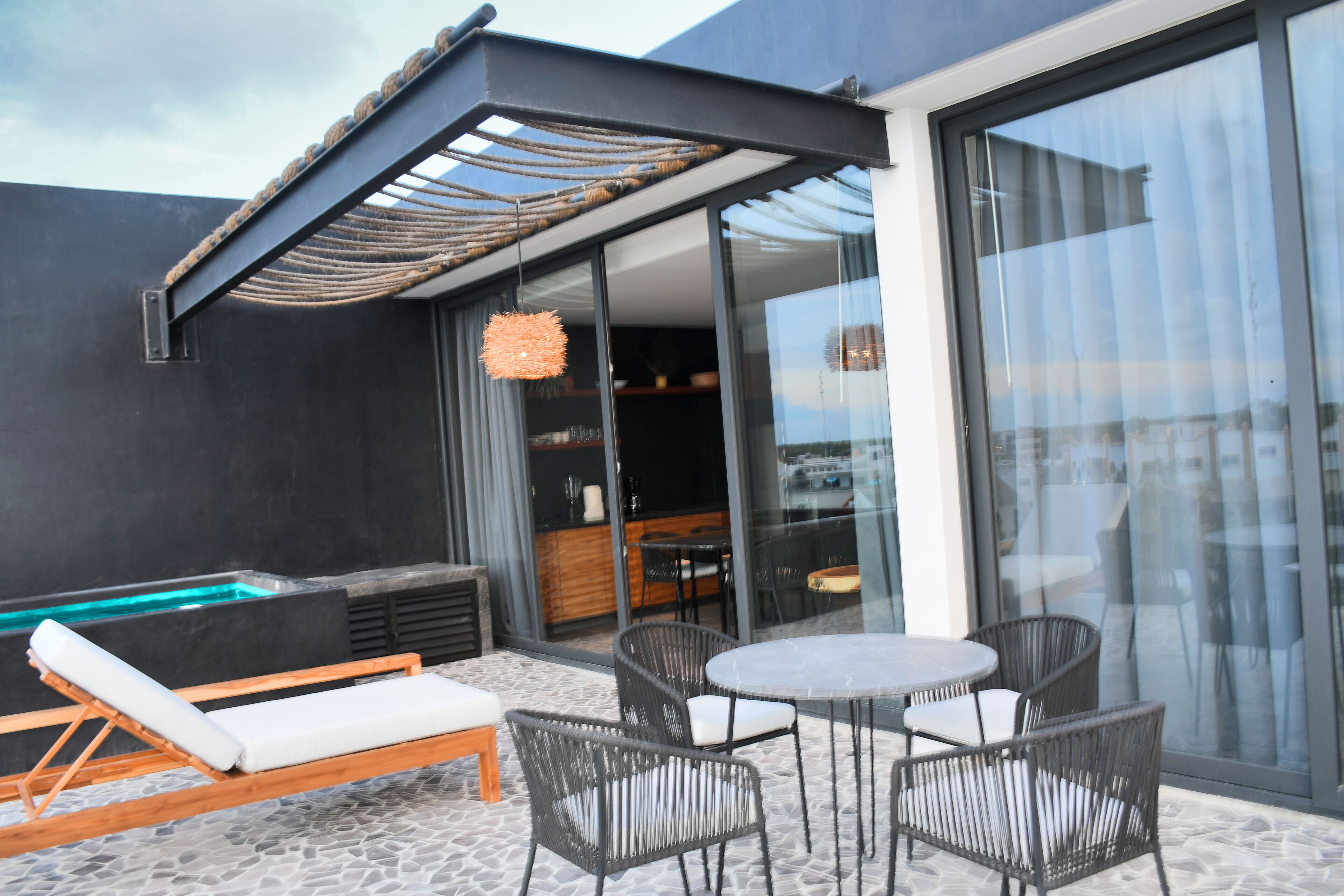Eine moderne Außenpatio mit einer Liege, Korbstühlen, einem runden Tisch und einem durch Glas geschützten Bereich.