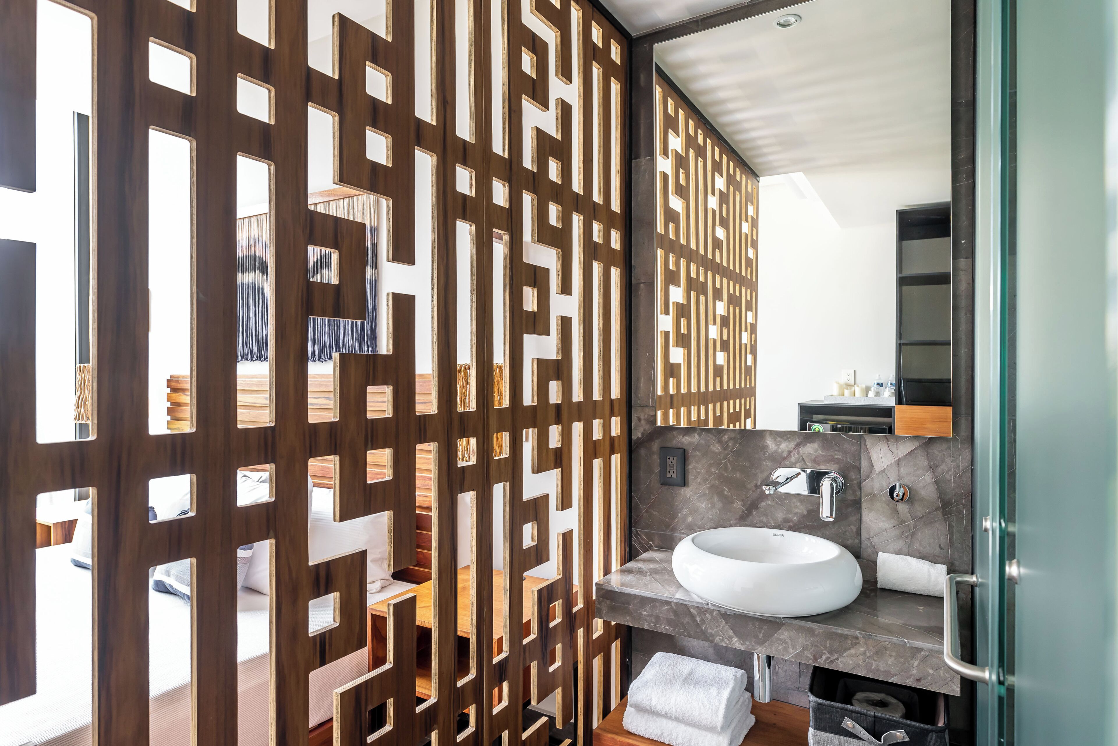 Un baño moderno con separador de madera, un lavabo redondo y un espejo.