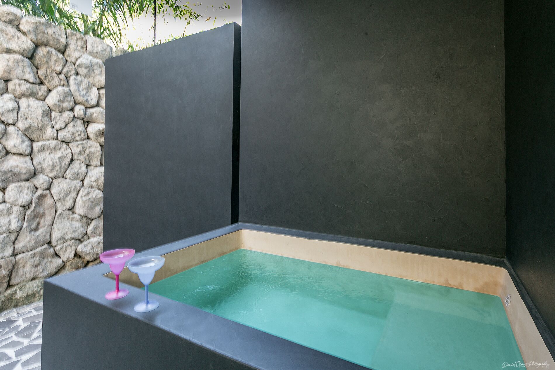 A spa area with a stone wall, a black partition, and a small pool with a pink and blue glass.
