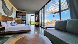 A modern hotel room with a large bed, a sofa, a wooden coffee table, and a view of the city through large windows. - IIK Tulum by The Spot Rentals (Tulum)