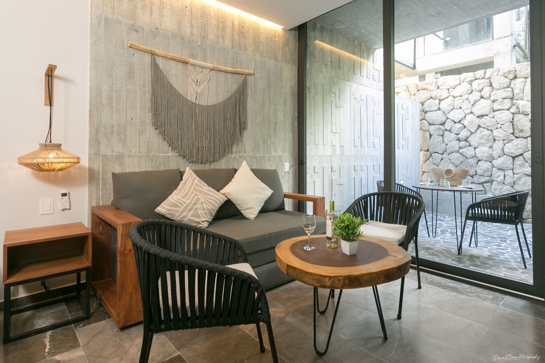Una sala de estar moderna con un sofá, dos sillones de mimbre negro, una mesa de centro de madera y una lámpara colgante.