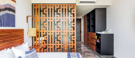 A hotel room with a bed, a wooden partition, a hanging light fixture, and a minibar.