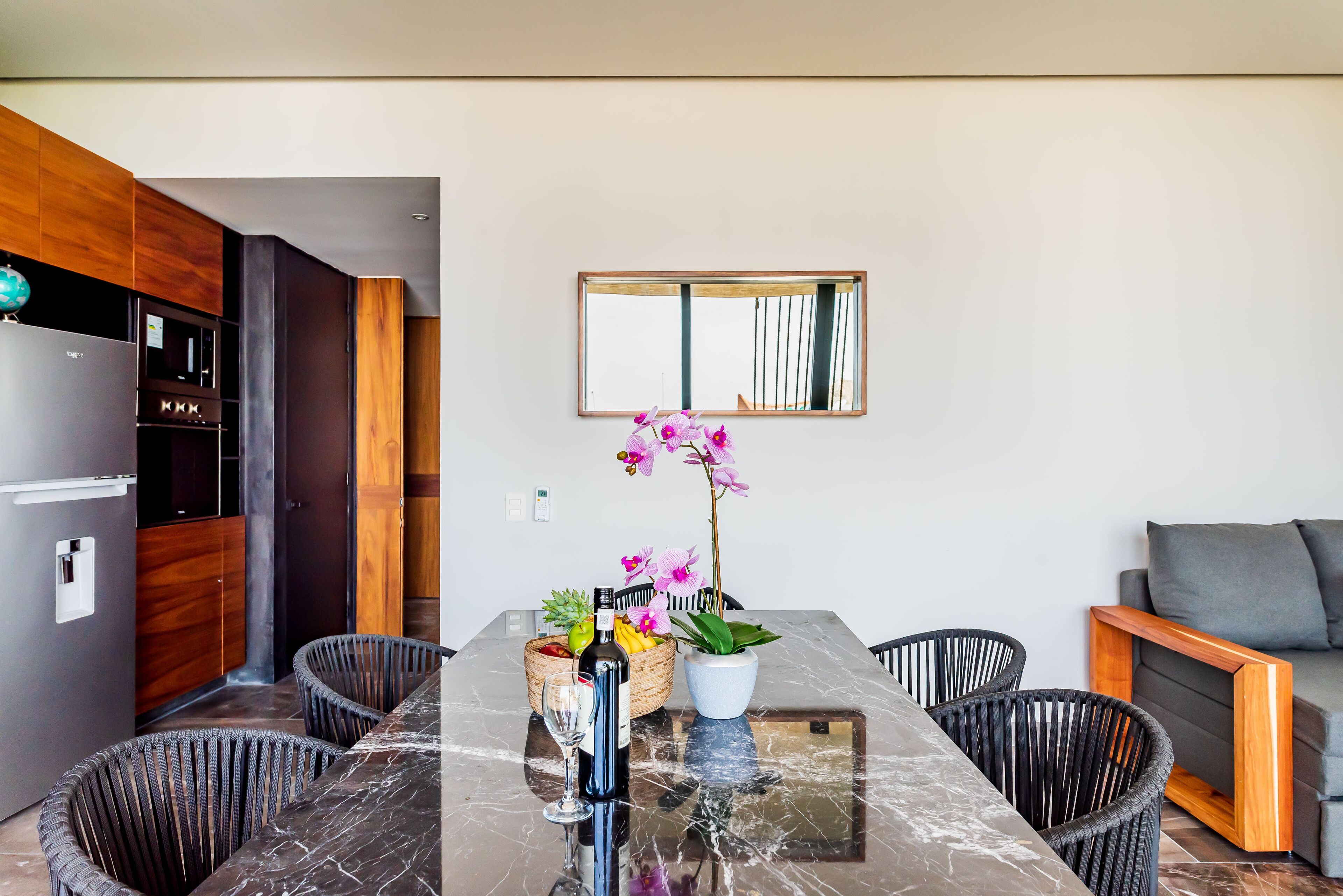 A modern kitchen with a marble countertop, a dining table with wicker chairs, a potted orchid, and a built-in oven.