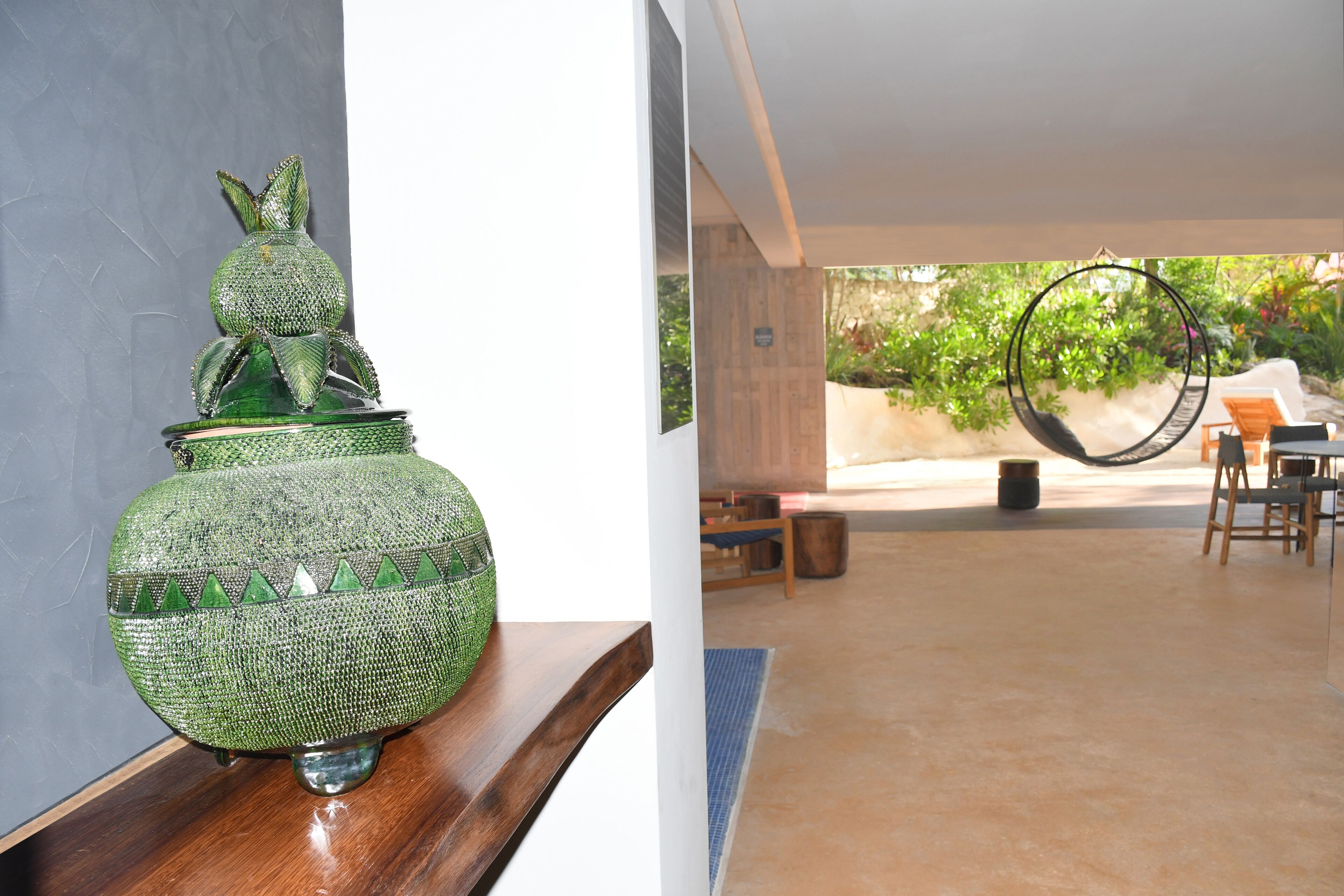 Un vase décoratif vert posé sur une étagère en bois, un hamac et un espace patio avec des chaises et une table.