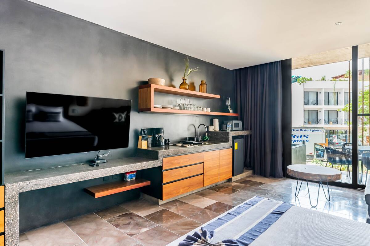 A modern kitchen with a flat-screen TV, wooden cabinets, and a dining area with a round table.