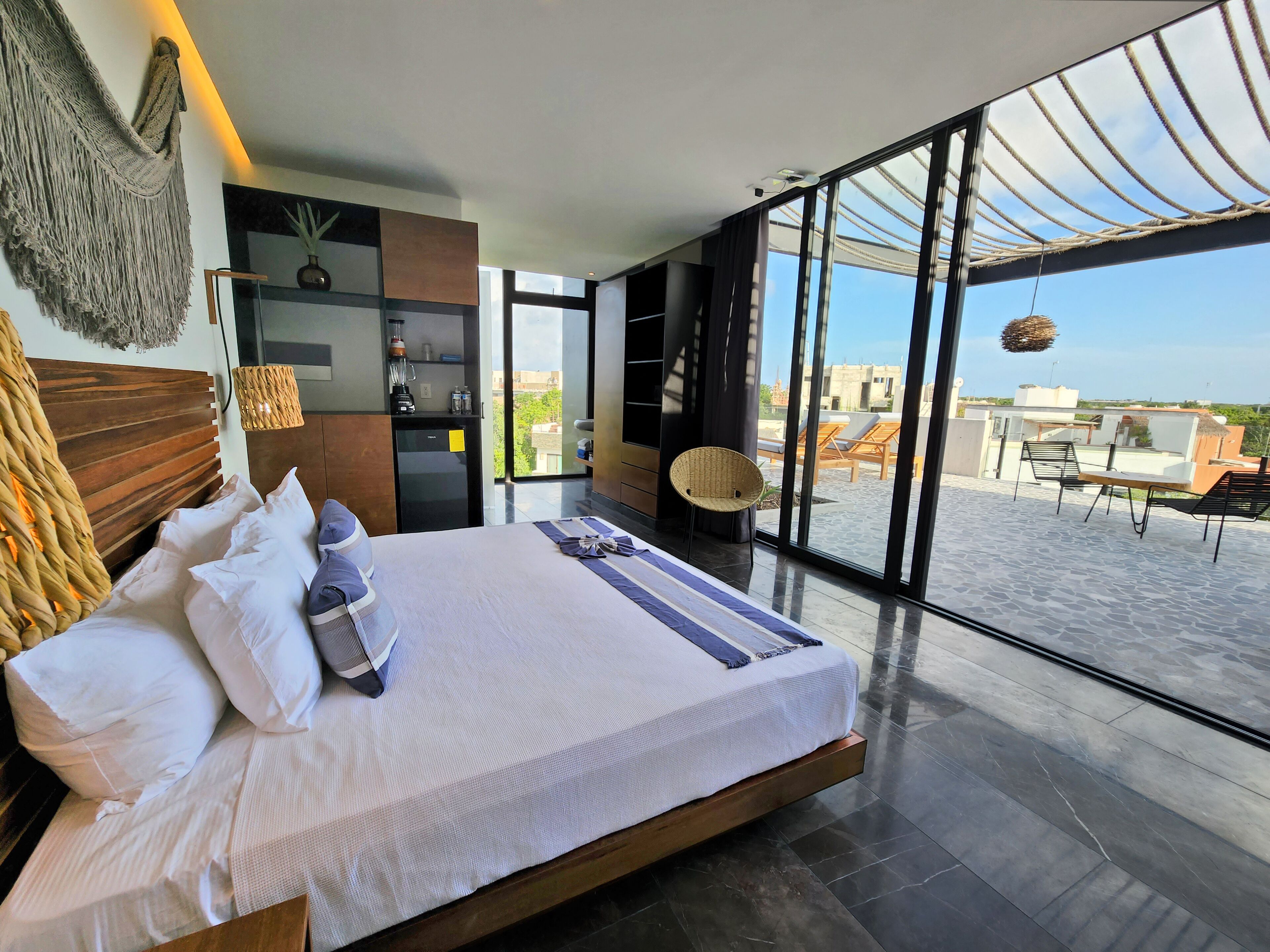 A modern bedroom with a large bed, a kitchen area, and a balcony with outdoor seating.