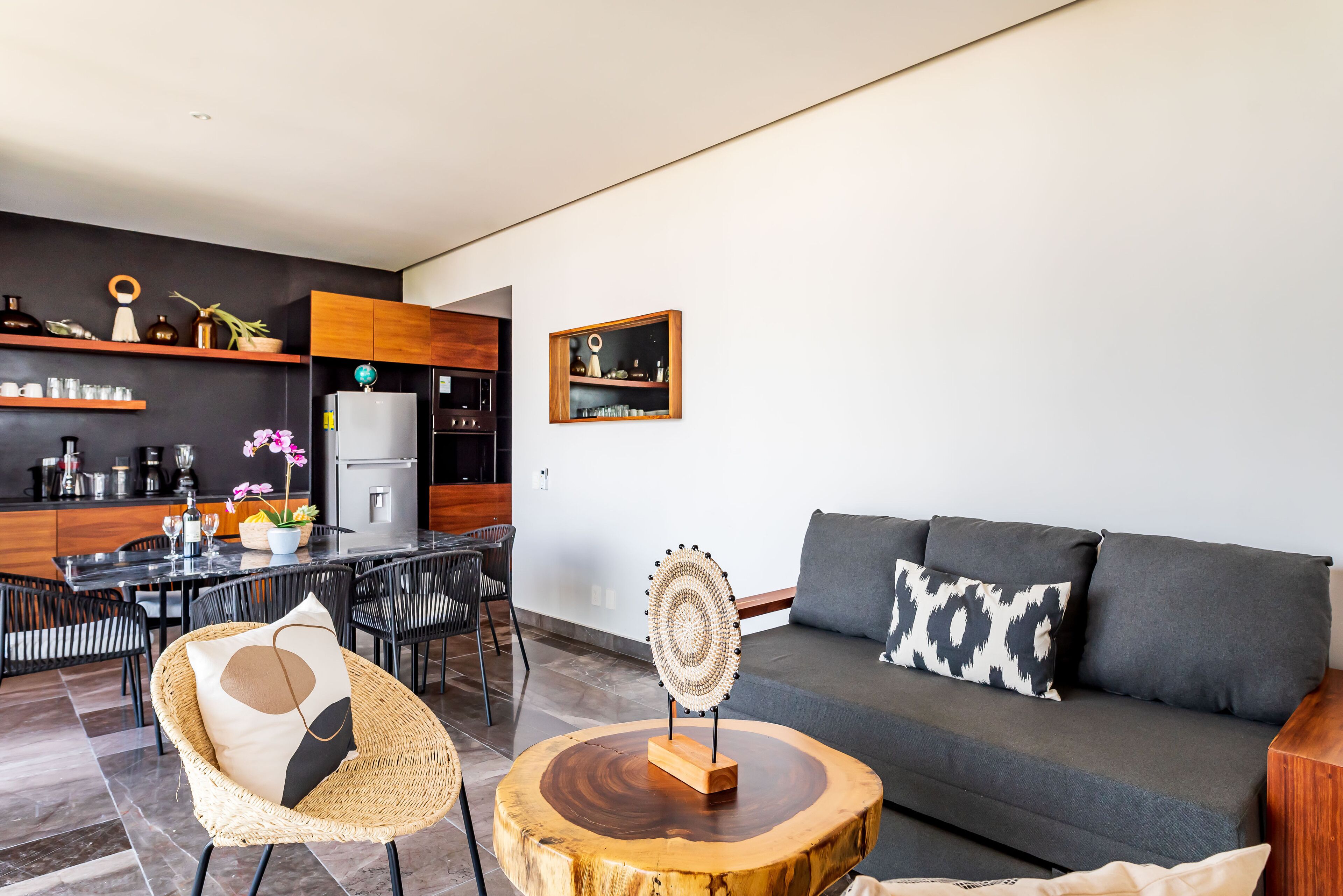 A modern living room with a grey sofa, a round wooden coffee table, and a dining area with a black table and chairs.
