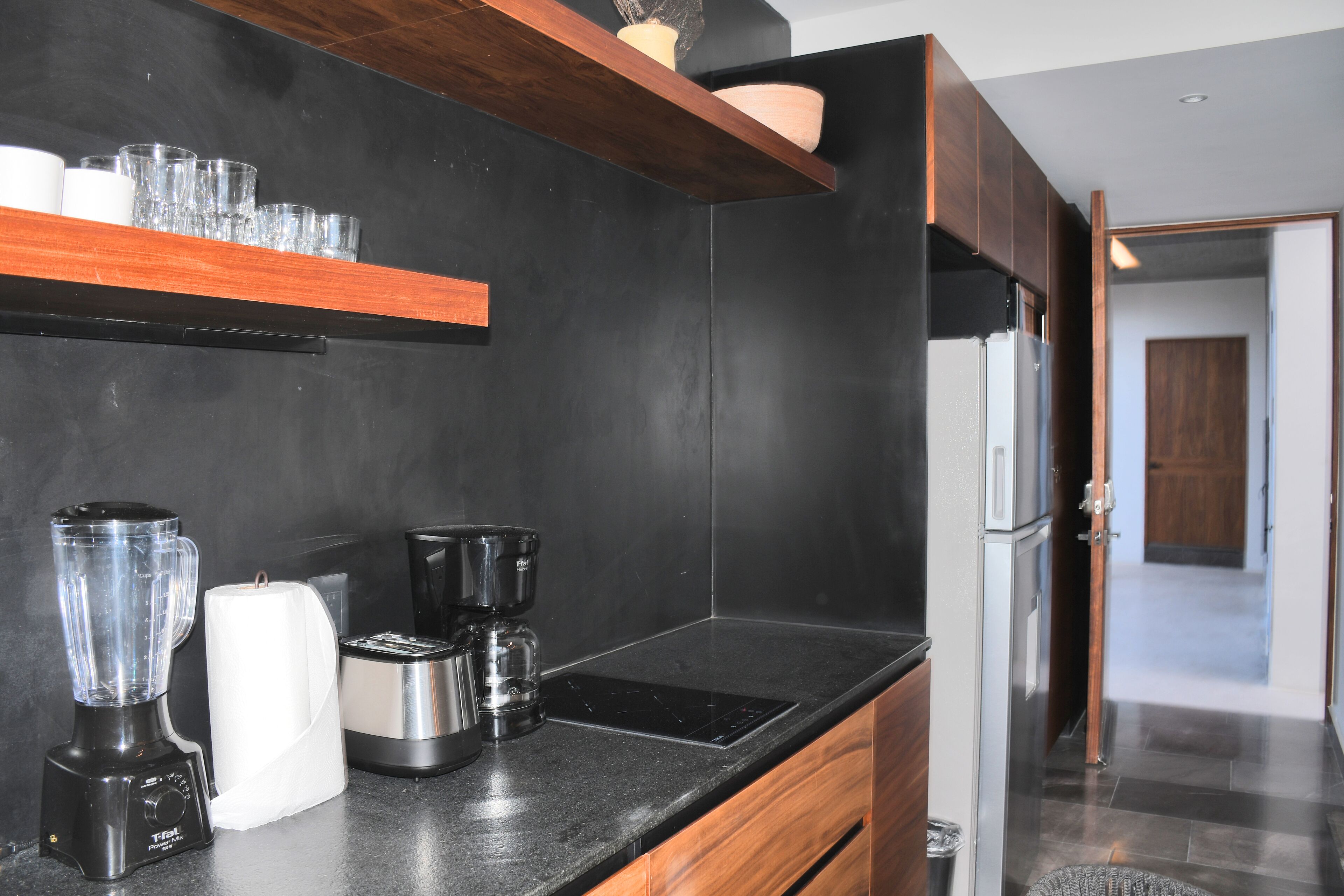 A modern kitchen with a black countertop, wooden cabinets, a built-in oven, and a coffee maker.