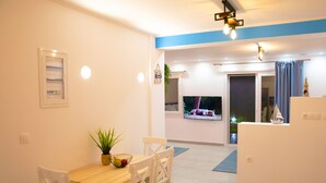 A dining area with a wooden table and white chairs, a small plant, and a fruit bowl. - Gikas Apartments - Serenity Suite (Corfu)